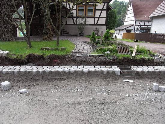 Barrierefrei, trotz Straßenabsenkung
Nachdem die Flusskante am Straßenrand gepflastert ist, kann man sehen was mit dem Grundstückszugang passiert. Die Straße liegt jetzt tiefer und es entsteht ein Absatz von mehr